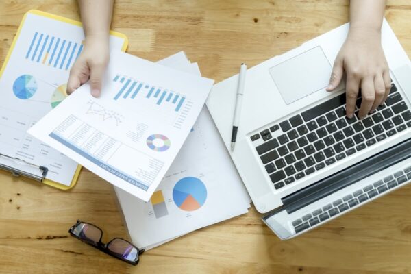 Na biurku widać laptop i dokumenty finansowe, które mogą pomóc przy ocenie, jaki jest koszt zatrudnienia księgowej.