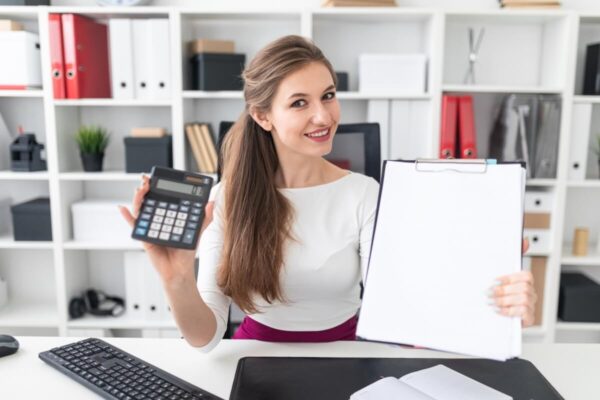 Kobieta w biurze prezentuje kalkulator i dokumenty związane z obsługą księgową.