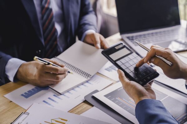 Na obrazie widać dwóch mężczyzn omawiających dokumenty i korzystających z kalkulatora, co symbolizuje kompleksowe zakładanie spółek.